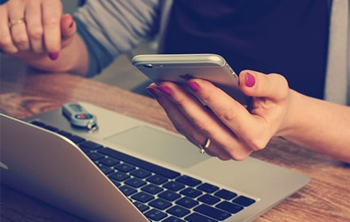 Hand holding mobile next to laptop